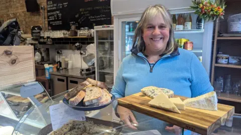 Sonia Johnson Sonia Johnson smiling wearing a blue top, while stood in her bakery behind the bread counter