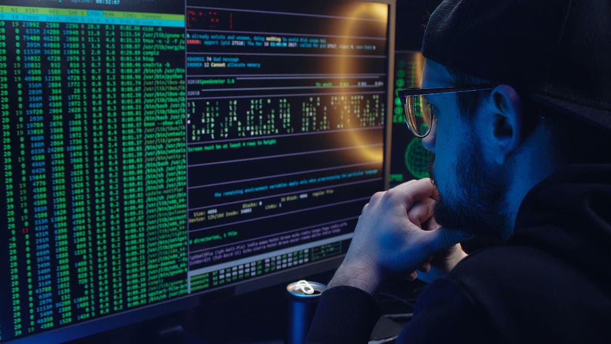 Hacker looks at computer code while sitting in a dark room